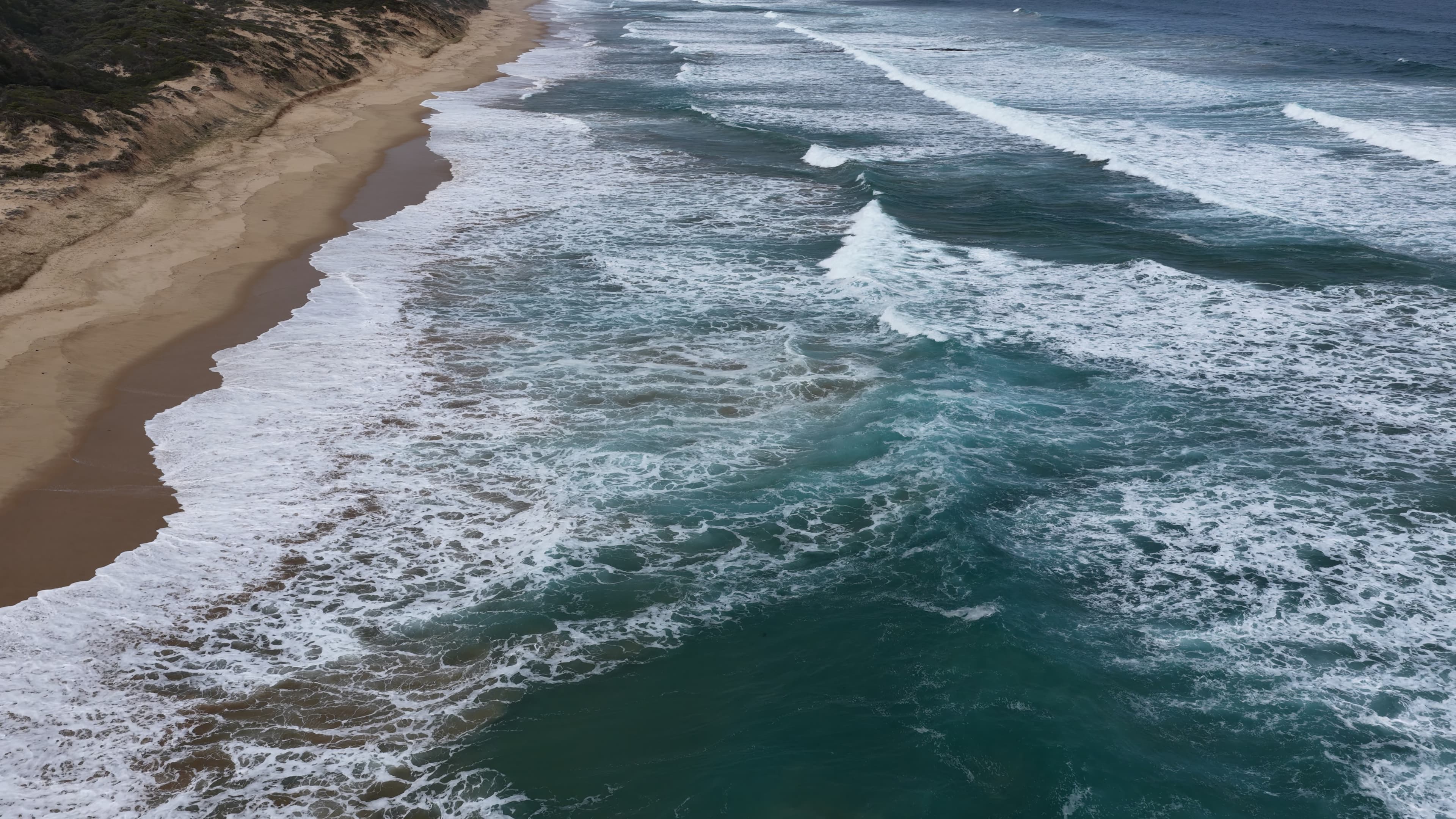 Turquoise waves rolling onto a California-style beach shoreline, seen from above